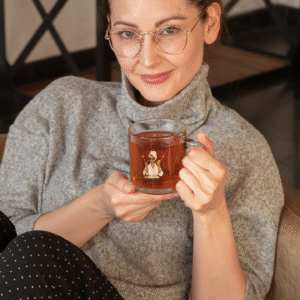 PerfectnElite Radiant & Chic clear glass mug featuring a stylish woman in a robe, held by a woman in cozy loungewear enjoying tea at home.