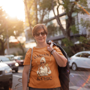Smiling woman wearing an orange “Radiant & Chic” T-shirt outdoors in sunlight, showing modern casual PerfectnElite fashion.