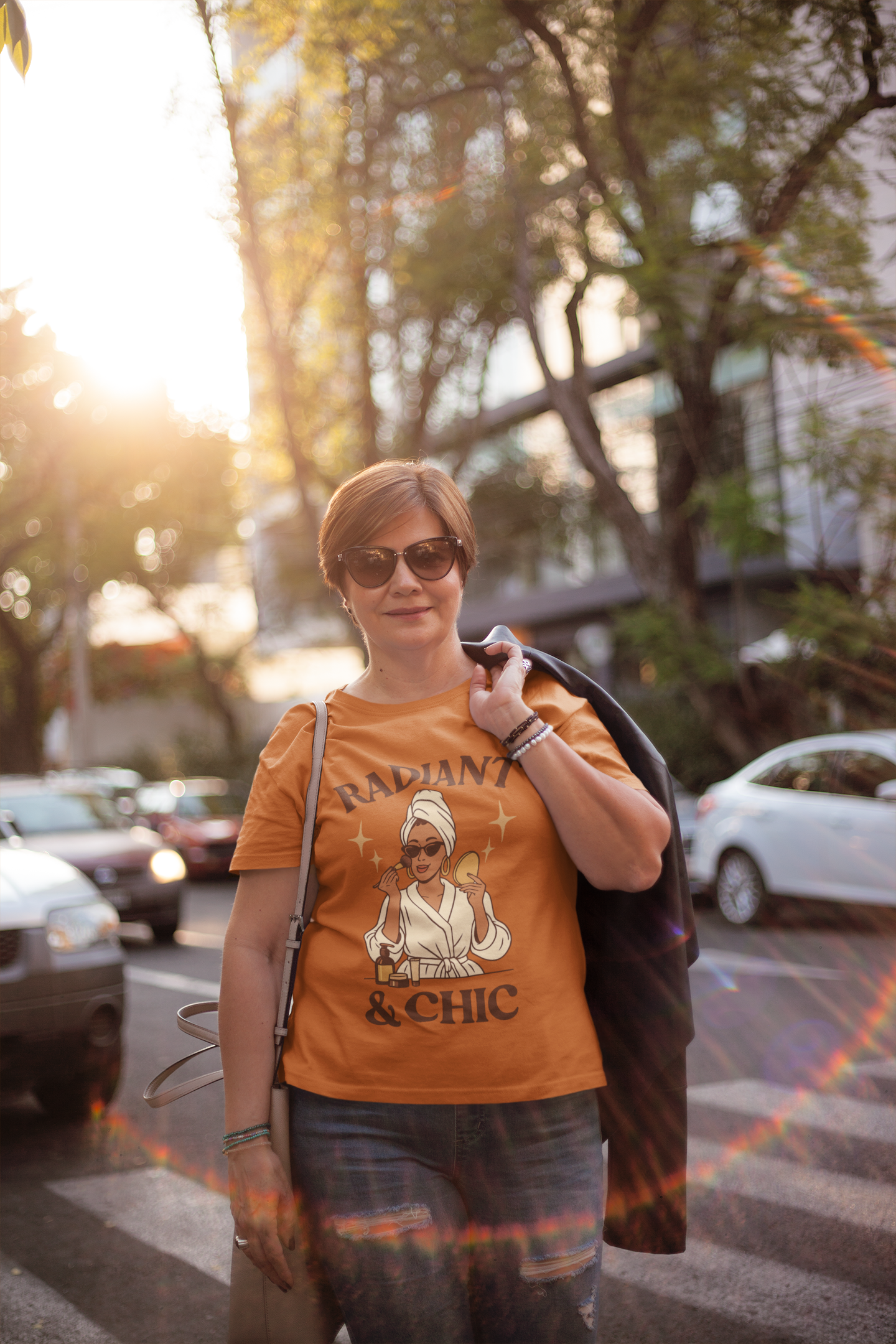 Smiling woman wearing an orange “Radiant & Chic” T-shirt outdoors in sunlight, showing modern casual PerfectnElite fashion.